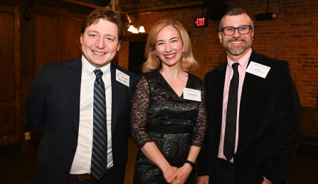 Two men and one woman smiling at a formal event. 