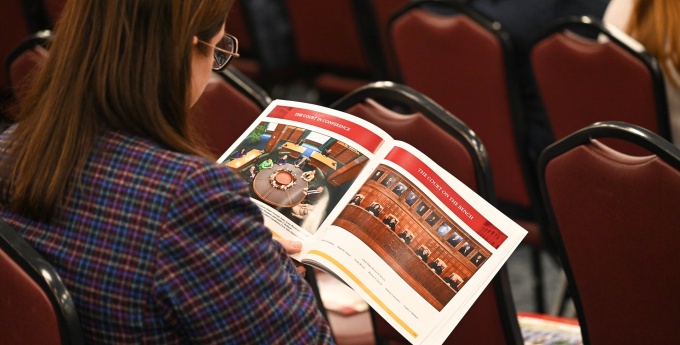 Individual sitting at a lecture, looking through a printed publication.