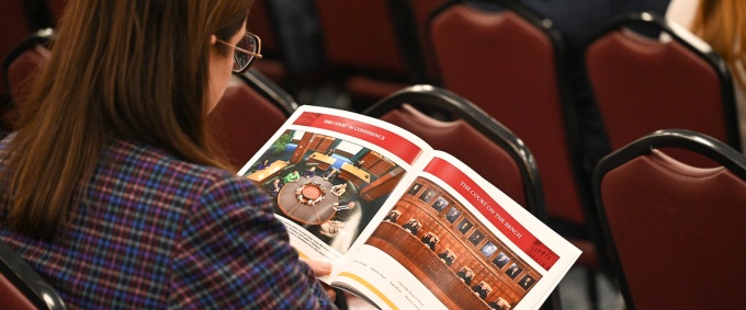 Individual sitting at a lecture, looking through a printed publication.