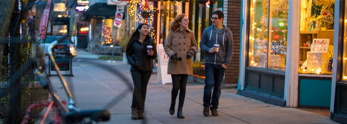 photo of three young adults walking down a sidewalk in the fall, talking and window shopping. 