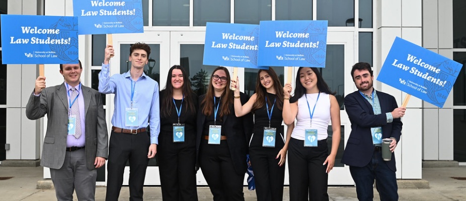 young adults standing outside in front of a building, holding signs that say "Welcome Law Students".