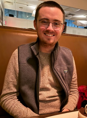 young man sitting at a restaurant table, smiling. 