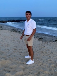 man smiling, standing on a sandy beach. 