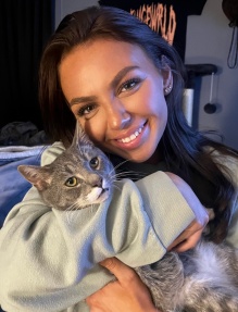 Young woman holding a cat in her arms, smiling. 