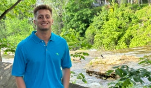 man smiling, standing outside next to a stream. 