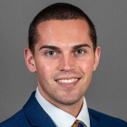 young man smiling, wearing blue jacket and tie. 