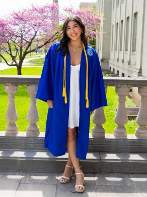 Young woman standing outside wearing graduation robe.