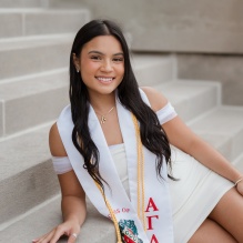 Young woman wearing white dress, sitting on steps of a building. 