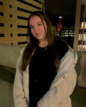 Young woman standing outside during the evening, wearing a white jacket. 