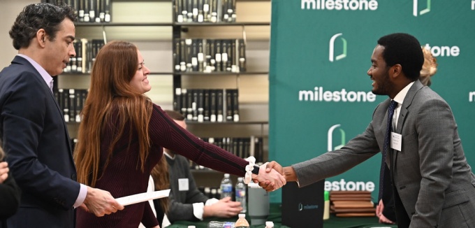 two individuals reachingn across table, shaking hands. 