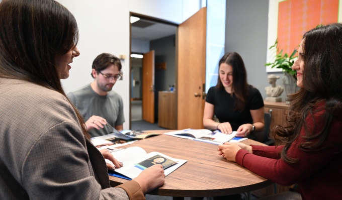 Group of students sitting at a round table, looking at Admissions materials.
