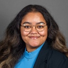 Woman with long hair, glasses, smiling. 