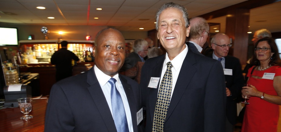 Two men wearing suits, smiling, attending a social event inside a bar. 