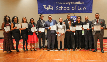 group of students standing under banner that says UB School of Law, holding up awards. 