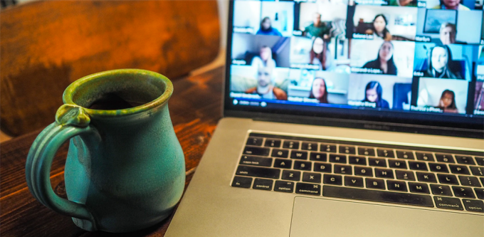 coffee mug sitting next to a computer, screen showing a zoom conference taking place.