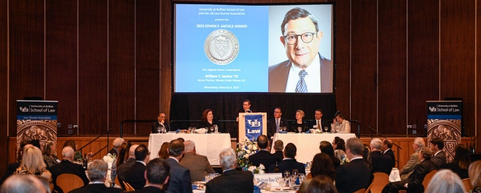 William Savino '75 stands at a podium, speakingn to a large group of people in a room. behind him is a screen that says 2023 Edwin F. Jaeckle Award with his photo.