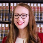 young woman smiling, standing in front of bookshelf with law books. 