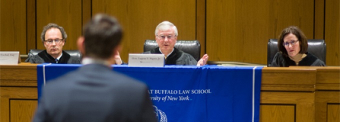 In a courtroom, man standing in front of a judges bench where judge addresses the young man. 