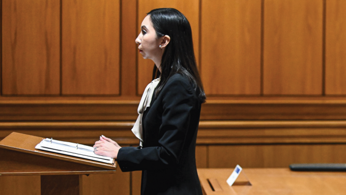 Woman in a courtroom standing at a podium. 