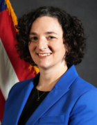 Fox-Solomon wearing blue jacket, U.S. flag behind her.