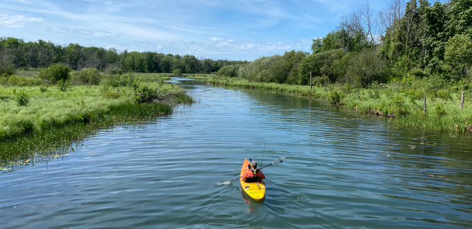 a person in a kaiyak, paddling down a blue channel on a sunny day.