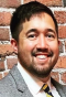 man smiling, standing in front of a brick wall. 