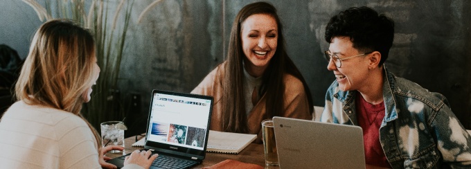photo of four people looking at a laptop screen in a library or coffee shop.