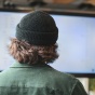 the back of a man's head with a hat on facing a computer screen. 