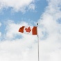 The Canadian flag waiving with the sky in the background. 