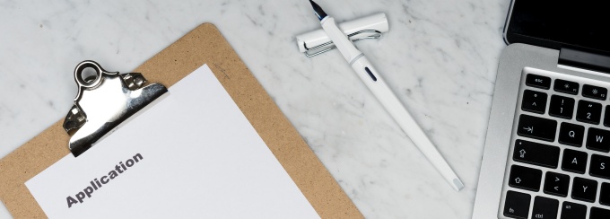 A clipboard with application, pen, and laptop on a marble table.