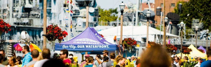 A crowd of people in front of Buffalo's Canalside side with Our City Our Waterfront pop-up tent.