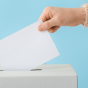 Woman's hand placing a slip of paper into a ballot box. 