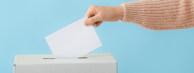 Woman's hand putting a slip of paper in a ballot box. 