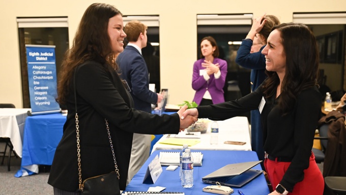 two women shaking hands across a table. 