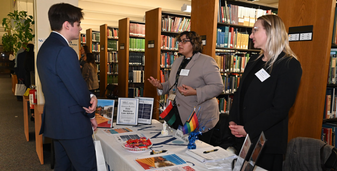 People attending career fair in the law library, standing at a table, talking. 