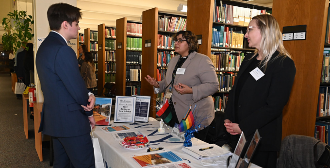 People attending career fair in the law library, standing at a table, talking.