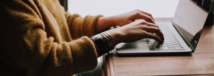 hands typing on a laptop sitting on a table next to a window.