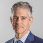 Man wearing blue jacket, tie, smiling. 