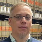 man wearing glasses standing in front of a bookcase with legal books. 