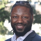 man wearing suit, smilling, standing outside.