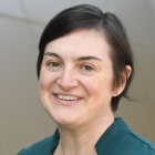 woman wearing green shirt, standing outside, smiling. 