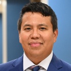 Man wearing suit. tie, standing in a hallway, smiling. 