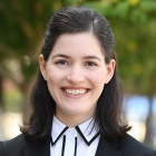 Woman wearing black and white suit, smiling, standing outside near some bushes. 