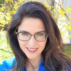 a woman wearing glasses and blue shirt standing outside. 