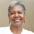 woman wearing white jacket, standing outside, arms crossed, smiling.