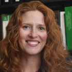 Woman standing, arms folded, in front of a bookcase with legal casebooks. 