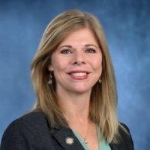 woman wearing black jacket, greet top, smiling. 