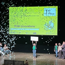 woman on a stage, holding up a giant check with confetti falling around her. 