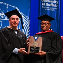 two men holding up a plaque during a graduation ceremony. 