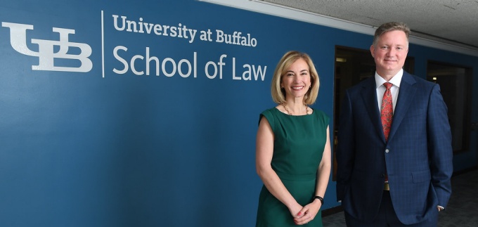 two people standing in front of a blue wall that says University at Buffalo School of Law. 